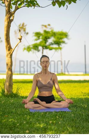 A Woman In Brown Sport Bra And Black Short Sitting On Yoga Mat Doing Maditation With Hand Together A