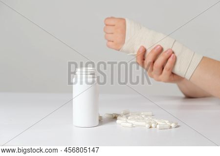 A Persons Hand With An Elastic Bandage And A Jar Of Calcium Or Chondroitin Tablets. Treatment Of Fra