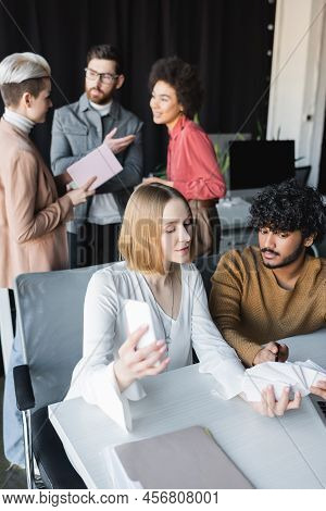 Indian Man Pointing At Samples Near Colleague And Interracial Team Talking On Blurred Background