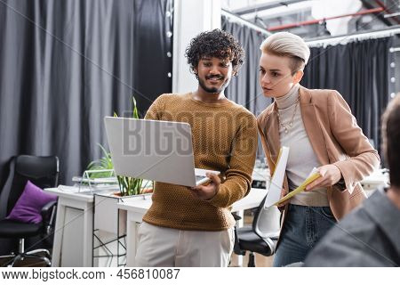 Happy Inidian Man Holding Laptop Near Woman With Folder In Advertising Agency