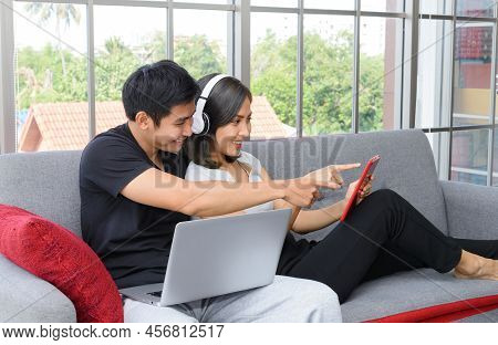 Young Asian Couple Wear Casual Clothing Relax Sitting On Cozy Couch In Living Room. Man Working On L