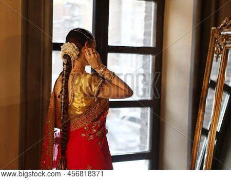 Female Model Indian Bride In Saree, Wearing Gold And Jasmine Flower Garlands In The Hair Near Mirror