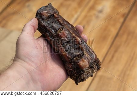 Dried Chew Treats For Dogs. A Man Is Holding A Dried Beef Tail In His Hand. A Piece Of Tail Against 