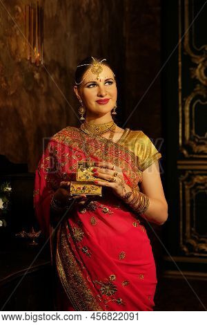 Charming Young Woman In Traditional Indian Red Sari And Jewelry Holding Golden Casket, Beautiful Wom