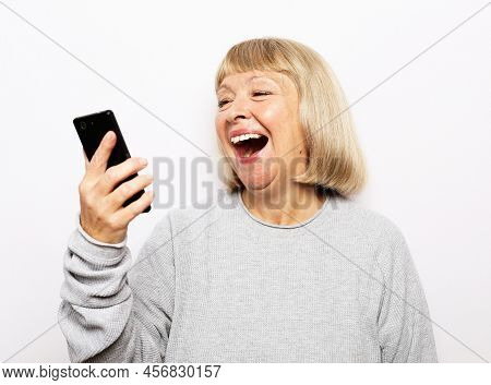 Portrait Of Attractive Blond Senior Woman Talking By Mobile Phone Over White Background