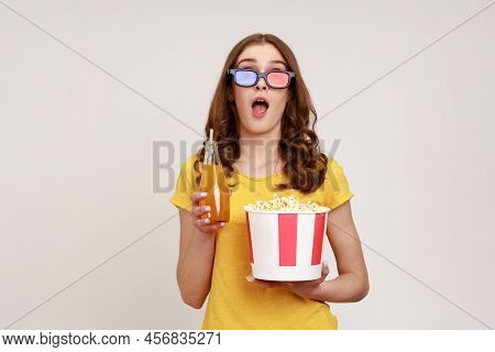 Portrait Of Amazed Wavy-haired Teenage Girl Wearing Eyewear And Yellow Casual Style T-shirt Eating C