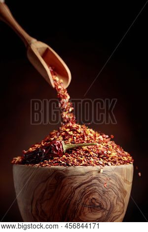Chilli Flakes Are Poured Into A Wooden Dish. Chilli Flakes And Dried Chili Peppers On A Brown Backgr