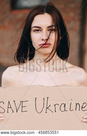 Close-up Portrait Of A Nude Woman With A Poster Save Ukraine. A Woman With A Belligerent Look. Stron