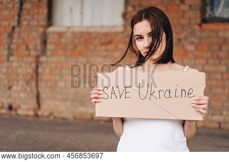 Women With Poster Save Ukraine. A Woman With A Belligerent Look Looks Into The Camera. Wind Develops