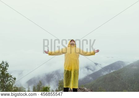 Happy Hiker Man Climbed To The Top Of The Mountain In The Rain, Raised His Hands Up And Rejoices Aga