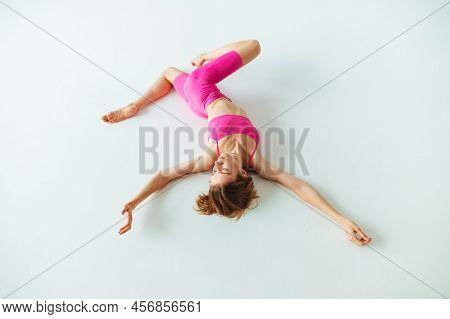 Athletic Woman Is Training On The White Ground Lying Down, Wearing A Stylish Pink Sports Suit. The W