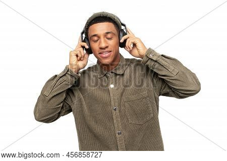 Studio Portrait Of Relaxed Cheerful Latin Man Wearing And Holding Wireless Headphones Isolated On Wh