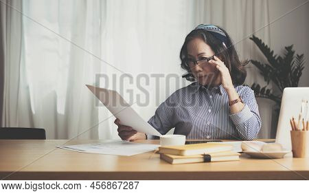 Seriously Senior Woman Tworking At Home, Looking At Laptop And Waving Paper Correspondence, Sitting 