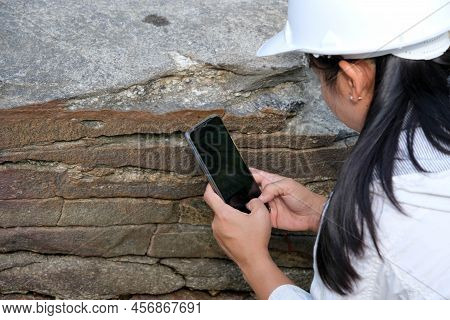 Asian Female Geologist Researcher Is Analyzing Rocks With A Smartphone In A Natural Park. Exploratio