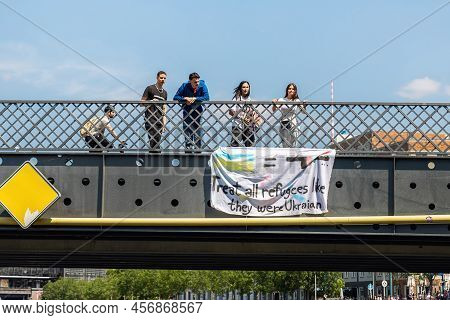 June 16th, 2022 - Berlin, Germany. Multiracial people stand on bridge with protest demonstration action holding poster Treat all refugees like they were Ukrainian. Racial migrants equalty demand.