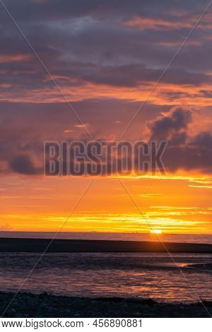 Sun Sets On Horizon Over Water Creating Beautiful Coloured Sky On New Zealand West Coast At Okarito.