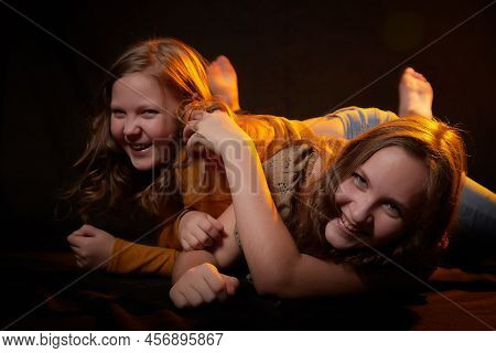 Two Cheerful Joyfull Sisters Having Fun Together In Dark Studio With Black Background