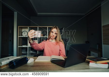 Positive Student Girl Taking Selfie While Studying At Home With A Smile On Her Face, Sitting At A Ta