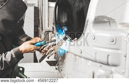 Worker In Protective Mask Welds Car Metal Elements Of Bodywork. Working With Carbon Dioxide Welding.