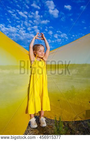 Ukrainian Girl 7 Years Old, She Is A Patriot Of Ukraine, Dressed In A Yellow Dress Against A Blue Sk