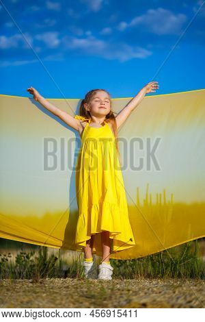Ukrainian Girl 7 Years Old, She Is A Patriot Of Ukraine, Dressed In A Yellow Dress Against A Blue Sk