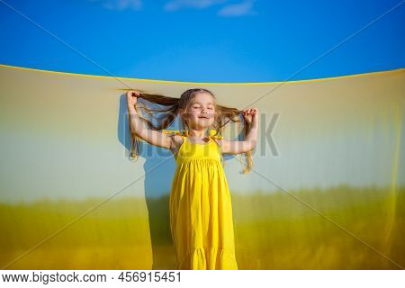 Ukrainian Girl 7 Years Old, She Is A Patriot Of Ukraine, Dressed In A Yellow Dress Against A Blue Sk
