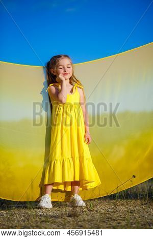 Ukrainian Girl 7 Years Old, She Is A Patriot Of Ukraine, Dressed In A Yellow Dress Against A Blue Sk