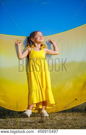 Ukrainian Girl 7 Years Old, She Is A Patriot Of Ukraine, Dressed In A Yellow Dress Against A Blue Sk