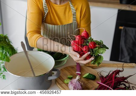 Unrecognizable Woman In Apron Holding Bunch Of Fresh Juicy Radish And Sliced Cucumbers Near Pan In K