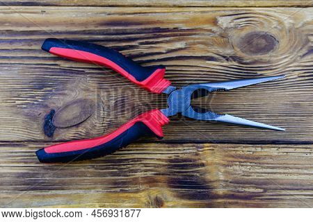 Needle Nose Pliers With Red Handles On Wooden Background. Top View