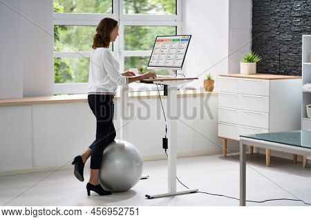 Woman Using Adjustable Height Standing Desk In Office For Good Posture