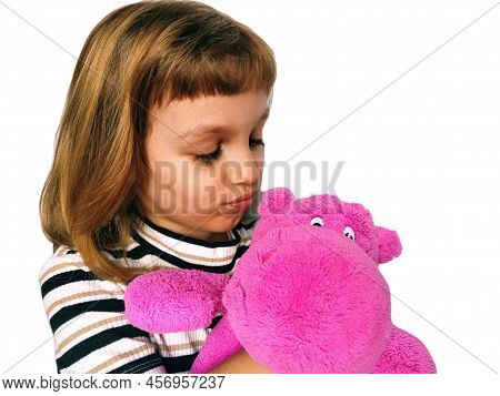 A Cute Caucasian Girl Of 7 Years Old With Blond Hair Cuddles And Hugs A Pink Hippopotamus. Hippo Plu