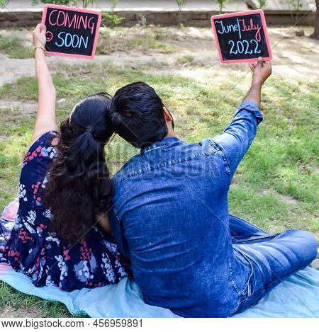 Indian Couple Posing For Maternity Baby Shoot. The Couple Is Posing In A Lawn With Green Grass And T