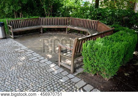 Arch Of The Flowerbed Surround The Wooden Bench In The Park. The Bench Is Bent Like A Horseshoe, Wit