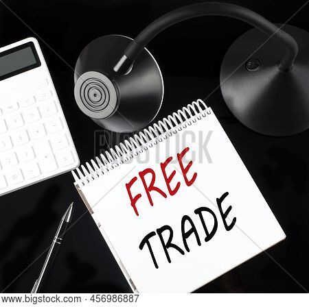 Opened Paper Notebook With Text Free Trade With A Pen, Calculator And Table Lamp On A Black Backgrou