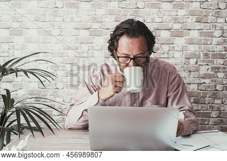 Man Using Computer At The Desk In Home Office Work Place. Young Mature Caucasian People Looking Lapt
