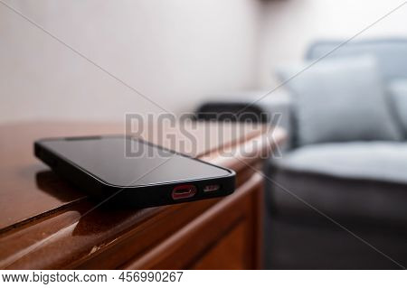 Smartphone Is Inadvertently Left On The Edge Of A Wooden Table And May Fall. Concept Of Careless Att