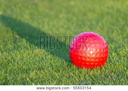 Red golf ball with shadow on grass