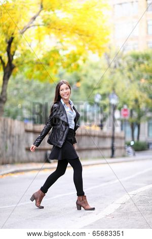Fashion urban young woman living city lifestyle walking in leather jacket crossing streets in full length in autumn fall. Trendy modern female. Multiracial Asian Caucasian model.