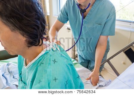 Cropped image of female nurse examining patient's back with stethoscope on bed in hospital