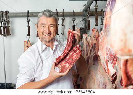 Portrait of happy mature male butcher holding fresh red meat in slaughterhouse