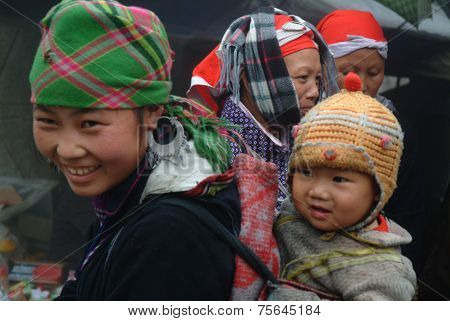 Hmong woman carrying child and wearing traditional attire.