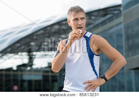 Athletic Mature Man Eating Bar Of Chocolate And Listening Music In The Urban Center