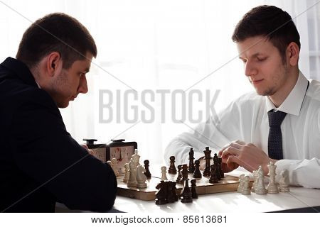 Two handsome businessmen playing chess in office