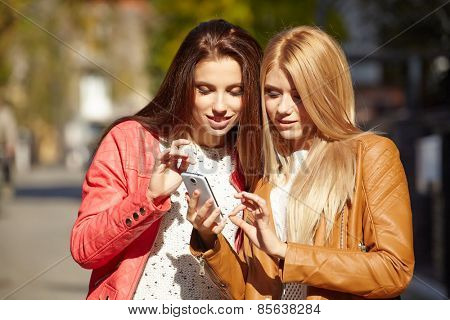  Two beautiful young womenlooking photos on smartfon.