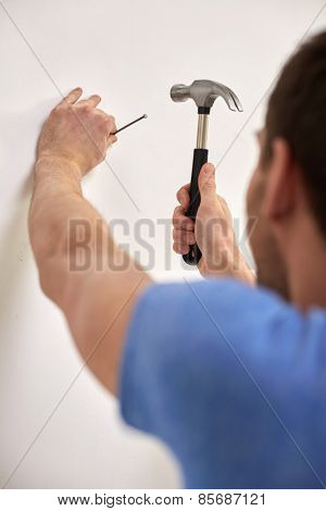 reapir, building, people and home renovation concept - close up of man with hammer hammering nail in wall