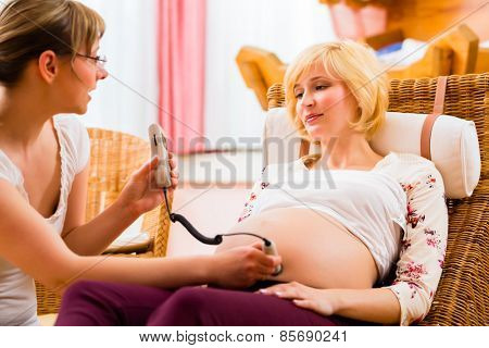 Midwife exanimating belly of pregnant woman with CTG scanning in practice