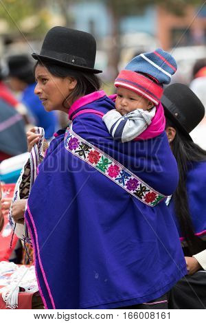 September 6, 2016 Silvia, Colombia: Guambiano indigenous woman dressed in colourful clothing carrying a toddler on her back