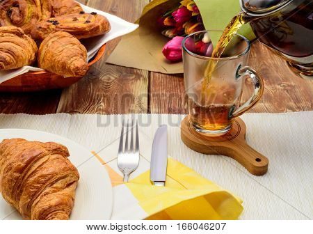 Tea with croissants , tulips, bake, pouring, cup, fork, knife, plate
