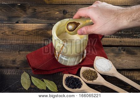 man prevents the spices in a mortar on a wooden background